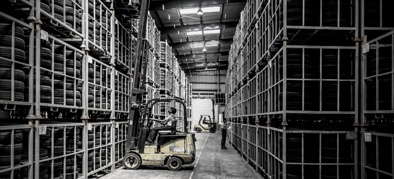 Rows of shelving in a technical warehouse interior with items being moved by a fork-lift truck